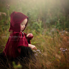 A young child in a red cape delicately touching a flower