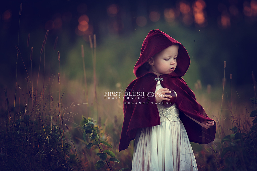 A young girl walking though the tall grass wearing a red cape