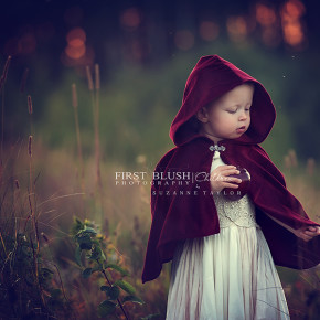 A young girl walking though the tall grass wearing a red cape