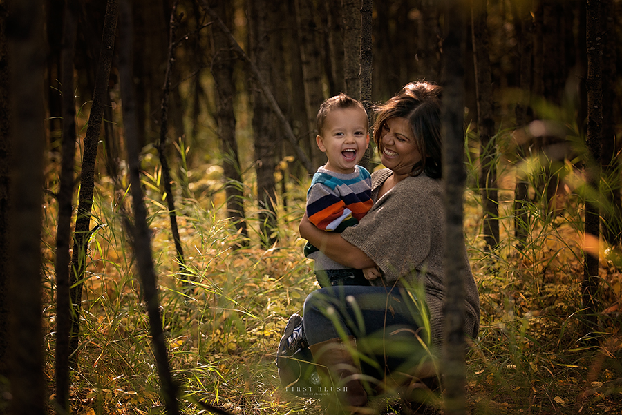 Mom hugging toddler son in a clearing.