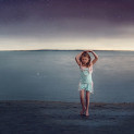 Young girl practices ballet on the beach at dusk with stars above her.