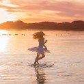 A young girl at sunset at Gull Lake in Alberta spins on one foot in the water wearing a tutu dress.