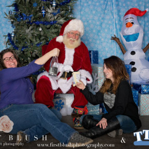 Santa sitting with two female volunteers sharing cookies and a bottle of wine at the 2015 TTMAC Christmas Party.