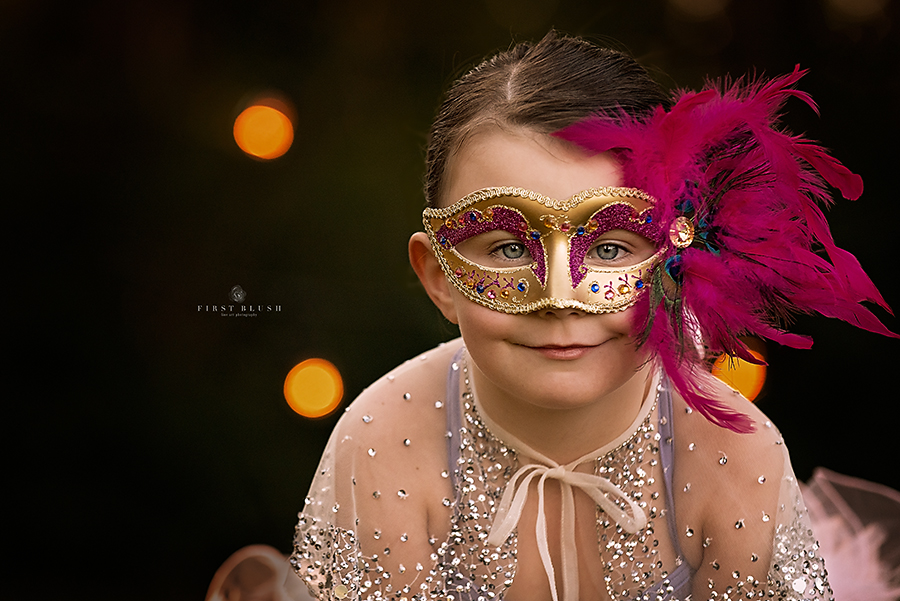 Child wearing Mardi Gras mask with pink feathers smiles at the camera using Make them smile Philosophy.